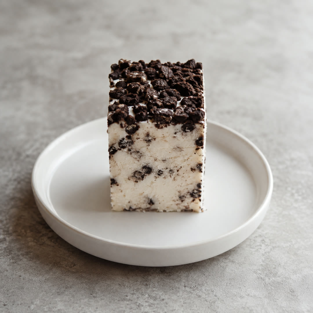 Uma barra de iogurte grego congelado em pé no prato branco, com a camada de biscoito de chocolate visível no corte
