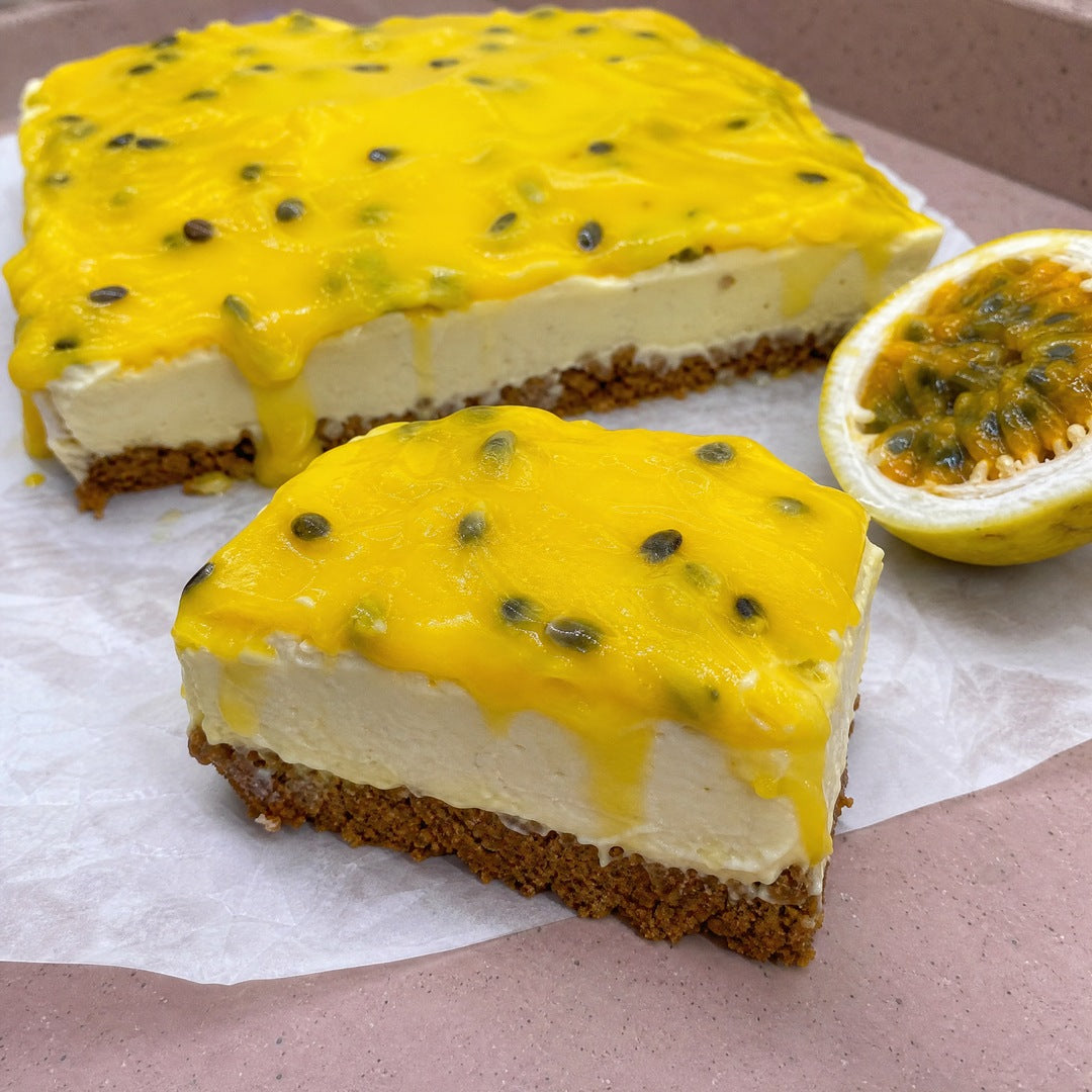 Fatia de torta de maracujá sobre papel manteiga, com base grossa de biscoito, creme claro e cobertura de maracujá escorrendo pela lateral