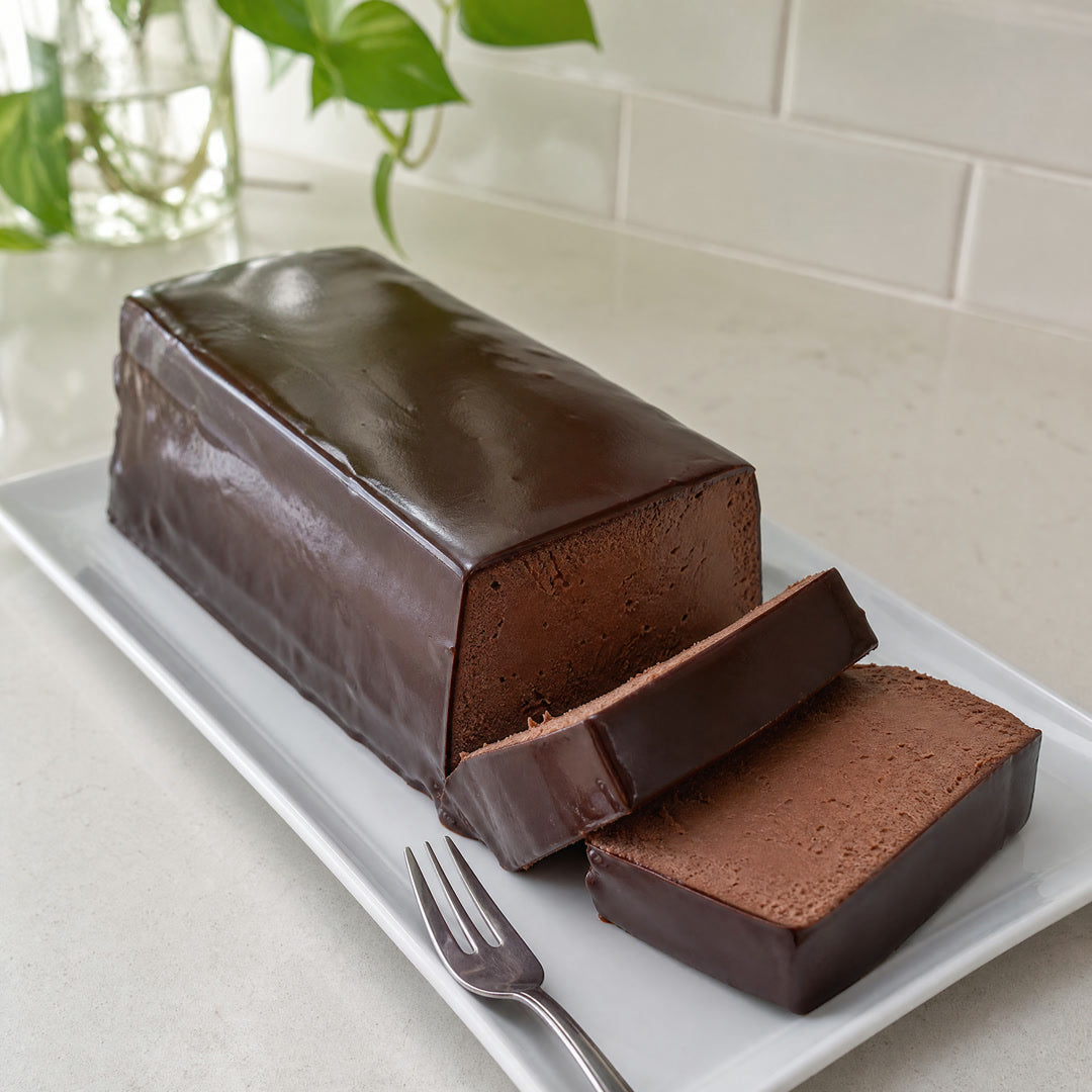 Mousse de chocolate enformada coberta de ganache, com duas fatias cortadas, sobre prato branco